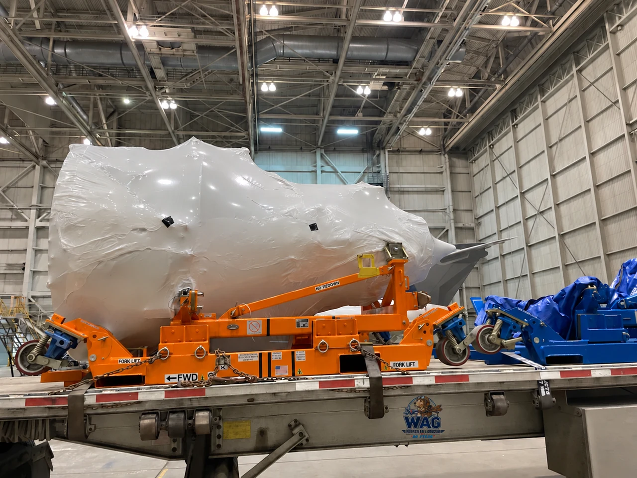 Wrapped jet engine on an orange transport stand on a trailer inside a hangar
