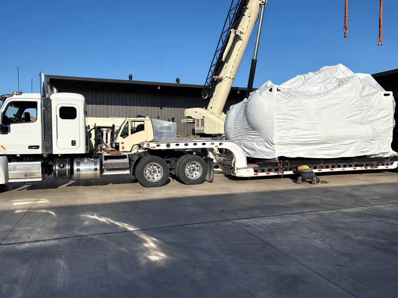 Worker beside the trailer securement of a wrapped chiller, with a crane and truck nearby